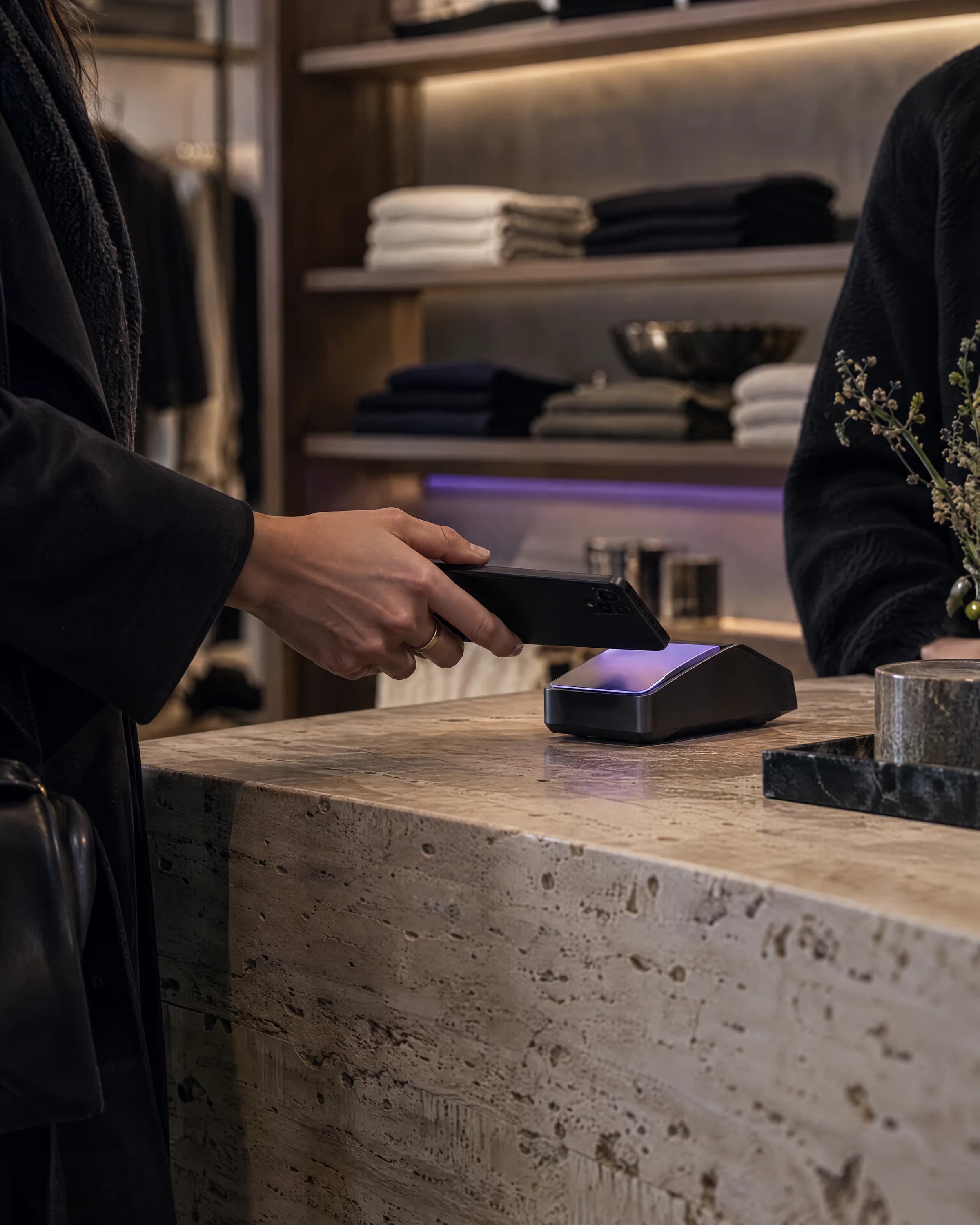 A customer taps a phone on a payment terminal at a stone shop counter.